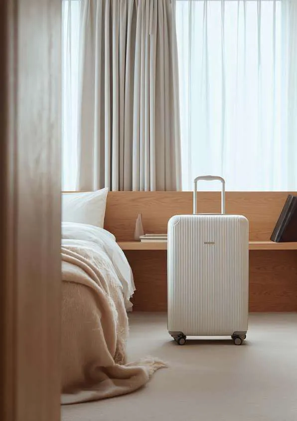 Bright hotel room with the bed made and a suitcase ready