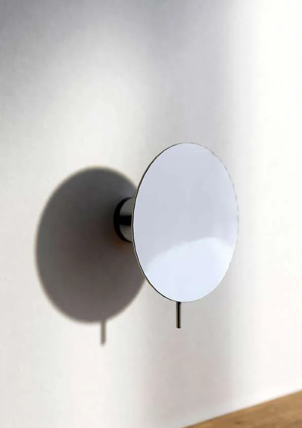 Round magnifying mirror mounted on the wall with a chrome arm